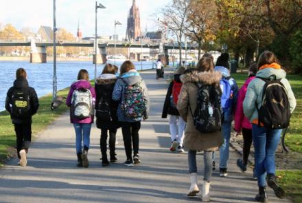 Auf dem Bild sieht man eines Schülergruppe auf einem geteerten Weg entlang eines Flusses laufen.
